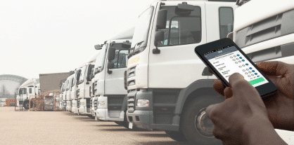 person with a phone looking at tms software with lorries in the back ground